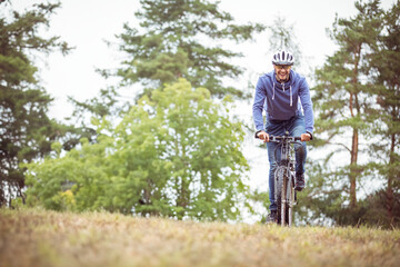 Fototapeta premium Mountain bike leaning on low grassy mound near dense pine and deciduous trees under overcast sky
