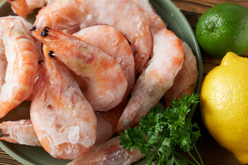 Frozen shrimps with lemon and parsley on wooden table, close-up.
