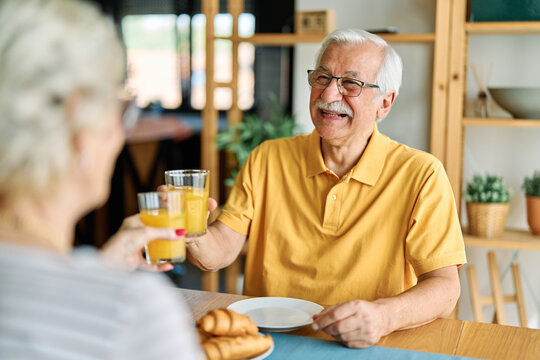 Portrait of an elderly senior couple having breakfast at home. Happy healthy affectionate senior couple eating and sitting at kitchen table having fun enjoying morning meal together - Powered by Adobe