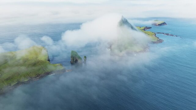 Aerial view of Drangarnir's majestic sea stacks piercing through the swirling mist, creating an ethereal and otherworldly vista, Drangarnir, Faroe Islands.