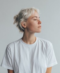 A person with short white hair poses confidently while wearing a simple white top. The plain background emphasizes their features and the calm atmosphere of the setting