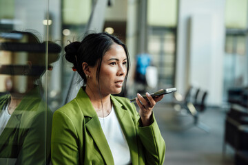 Businesswoman in green jacket speaking into smartphone in modern office