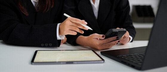 Two colleagues discussing data with smart phone and new modern computer laptop on desk table. Close up business team concept.