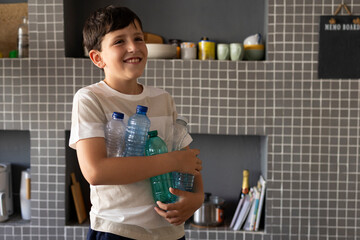 Grandson smiling in kitchen holding plastic bottles for recycling
