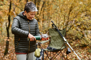 Naklejka premium Senior woman enjoys a peaceful moment cooking in the forest while hiking