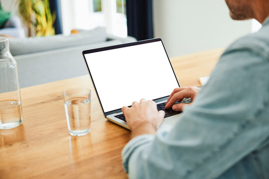 Person using laptop with blank screen mockup at home desk