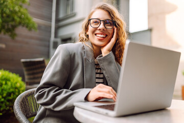Portrait of a woman wearing glasses with a laptop at an outdoor table. A businesswoman enjoys...