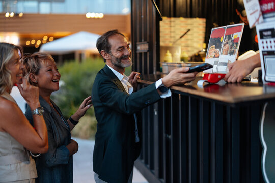 Businessman paying with smartphone at food truck with colleagues enjoying street food festival - Powered by Adobe