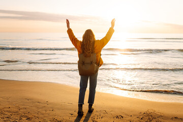 A beautiful woman with a backpack strolls along the shore at dawn. The traveler enjoys the seascape...