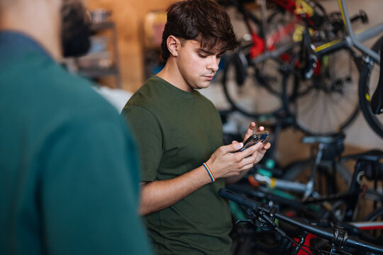 Bicycle shop worker using smartphone next to bicycles