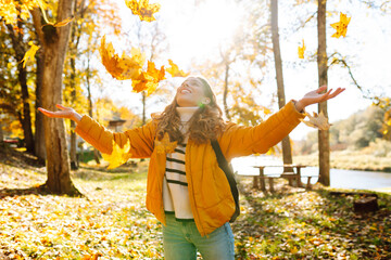 A sweet woman is having fun with fallen leaves in an autumn park. A beautiful woman tosses autumn leaves into the air at sunset. Concept of seasonality, fun, and relaxation.