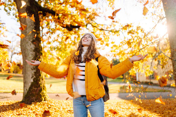 A sweet woman is having fun with fallen leaves in an autumn park. A beautiful woman tosses autumn leaves into the air at sunset. Concept of seasonality, fun, and relaxation.