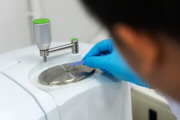 A laboratory technician carefully places a sample to the analysis plate of an FT-IR (Fourier Transform Infrared) spectrometer using tweezers prepared for precise material laboratory technology.