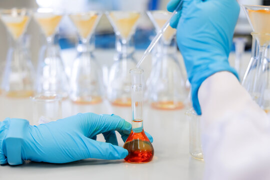 A scientist performs a borax detection test in a laboratory using an orange chemical solution inside a volumetric flask. Represents chemical analysis, food safety research in laboratory.