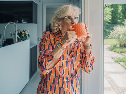 Woman in colorful shirt drinking coffee by kitchen doorframe