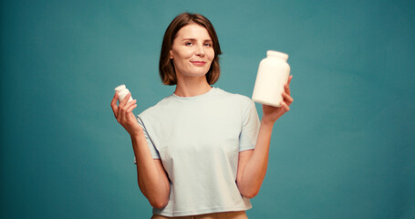 Beautiful young happy woman with choosing what vitamins to take on blue background