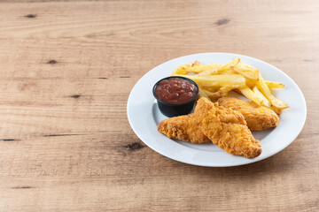 Crispy fried chicken tenders with french fries on wooden table. Copy space