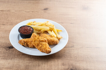 Crispy fried chicken tenders with french fries on wooden table. Copy space