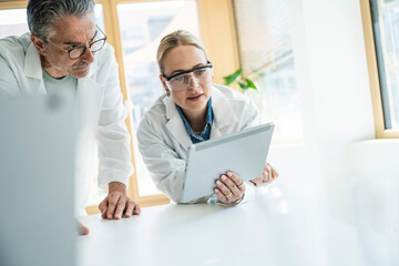 Scientists wearing lab coats working on tablet computer in laboratory