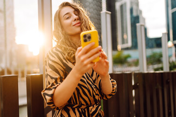 A young woman with a phone strolls along an alley against the backdrop of a cityscape. A beautiful...