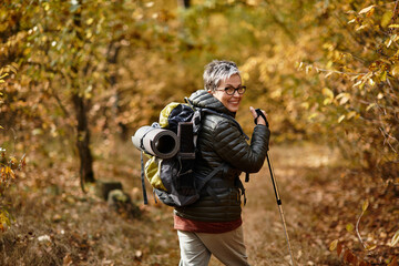 Naklejka premium Enjoying the tranquility of nature, a senior woman hikes through a vibrant autumn forest trail