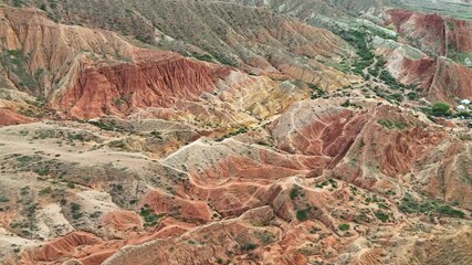 Aerial footage of Skazka Canyon in Kyrgyzstan as the drone steadily ascends, revealing the vast red rock formations and stunning mountain backdrop in warm daylight. - Powered by Adobe