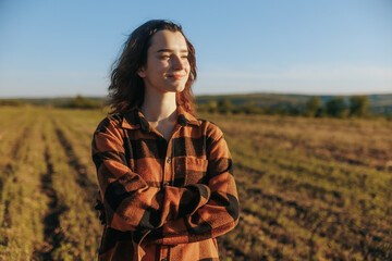 Young female farmer in plaid shirt standing in field during golden hour