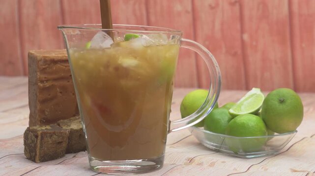close up stir crafted iced pitcher of Papel&oacute;n con Lim&oacute;n, a traditional Venezuelan beverage, with fresh limes and panela on the side