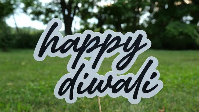 Message of the words Happy Diwali Floats on a Wooden Dowel In front of a Grassy Lawn with Trees in the Background at Sunset 4K Video