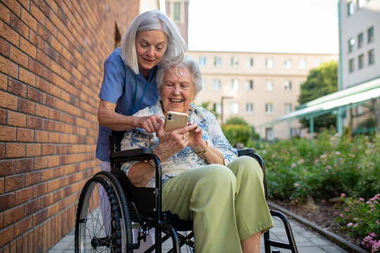 Senior patient in wheelchair showing picture in smartphone to caregiver.