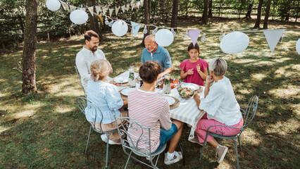 Areal view of grandparents, parents and kids dining together outside.