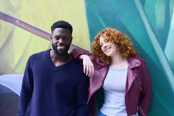 Interracial couple smiling and leaning against colorful graffiti wall