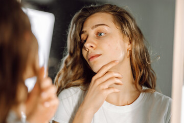 Beautiful woman touches her skin looking at her reflection in the mirror. Young woman enjoys...