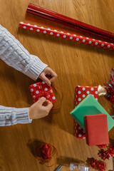 Hands wrapping a Christmas gift in red polka dot paper on wooden table, festive flatlay with copy space for holiday design or background