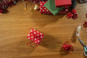 A festive pile of red and green wrapped Christmas gifts on a wooden table, surrounded by holiday decorations
