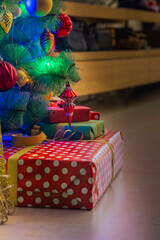 A vertical, low-angle shot of a stack of gifts under a Christmas tree with glowing lights and colorful ornaments