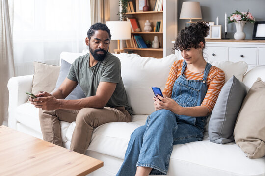 Jealousy and frustration. Young man is insecure, suffering from jealousy while his girlfriend is texting on her mobile phone. Smartphone and millennial generation. Online life.