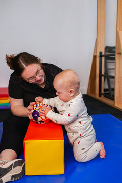 Baby kneeling on map reaching for a ball during physiotherapy appointment