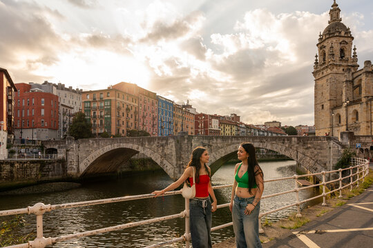 Two young women talking by the river in bilbao at sunset