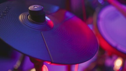 Close up of digital cymbal being struck by musician under vibrant studio lighting, showing motion and equipment detail during percussion practice with soft focus on surrounding background