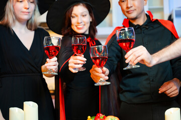 Halloween costumes toast with red wine at a festive indoor party. Pumpkins, food, and celebration set the mood for fun, spooky vibes and seasonal cheer.