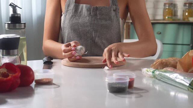 A woman peels garlic to prepare a spicy dish while sitting in a cozy kitchen.