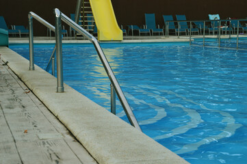 Fragment of a swimming pool with blue water and railings, handrails, fences.