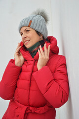 Caucasian woman in red down jacket and gray knitted hat on white background. Women's warm winter clothes.