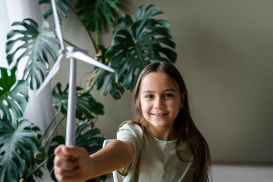 Girl holding wind turbine model by plants at home