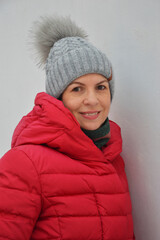 Portrait of pretty Caucasian woman in red winter jacket and grey knitted hat with fur pompom on white background. Women's warm street clothes.