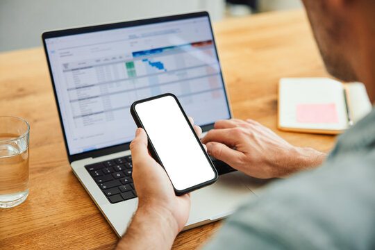 Person using smartphone and laptop for finance planning at workspace