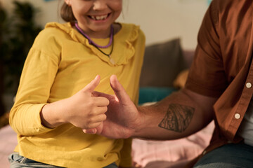 Caucasian child girl smiling while playing thumb wrestling game with adult Caucasian man, both hands visible with focus on interaction, man showing tattooed forearm, girl wearing necklace