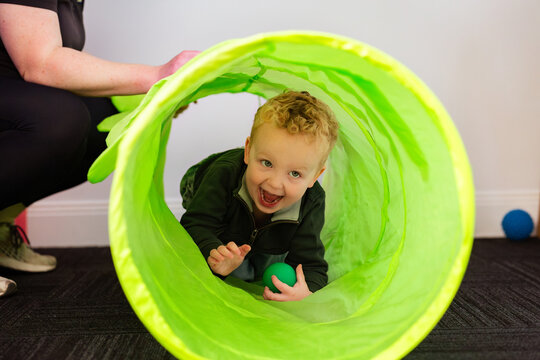 Toddler crawling through green tunnel as part of physiotherapy appointment assessment