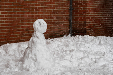 Snowman on a large blanket of snow. Brick wall background